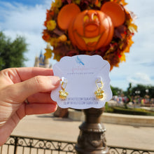 Load image into Gallery viewer, Gold pumpkin earrings held in front of a pumpkin and castle, with a blurred background
